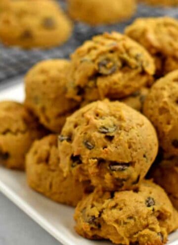 A plate of gluten free chocolate chip pumpkin cookies with more cookies on a wire rack in the background.