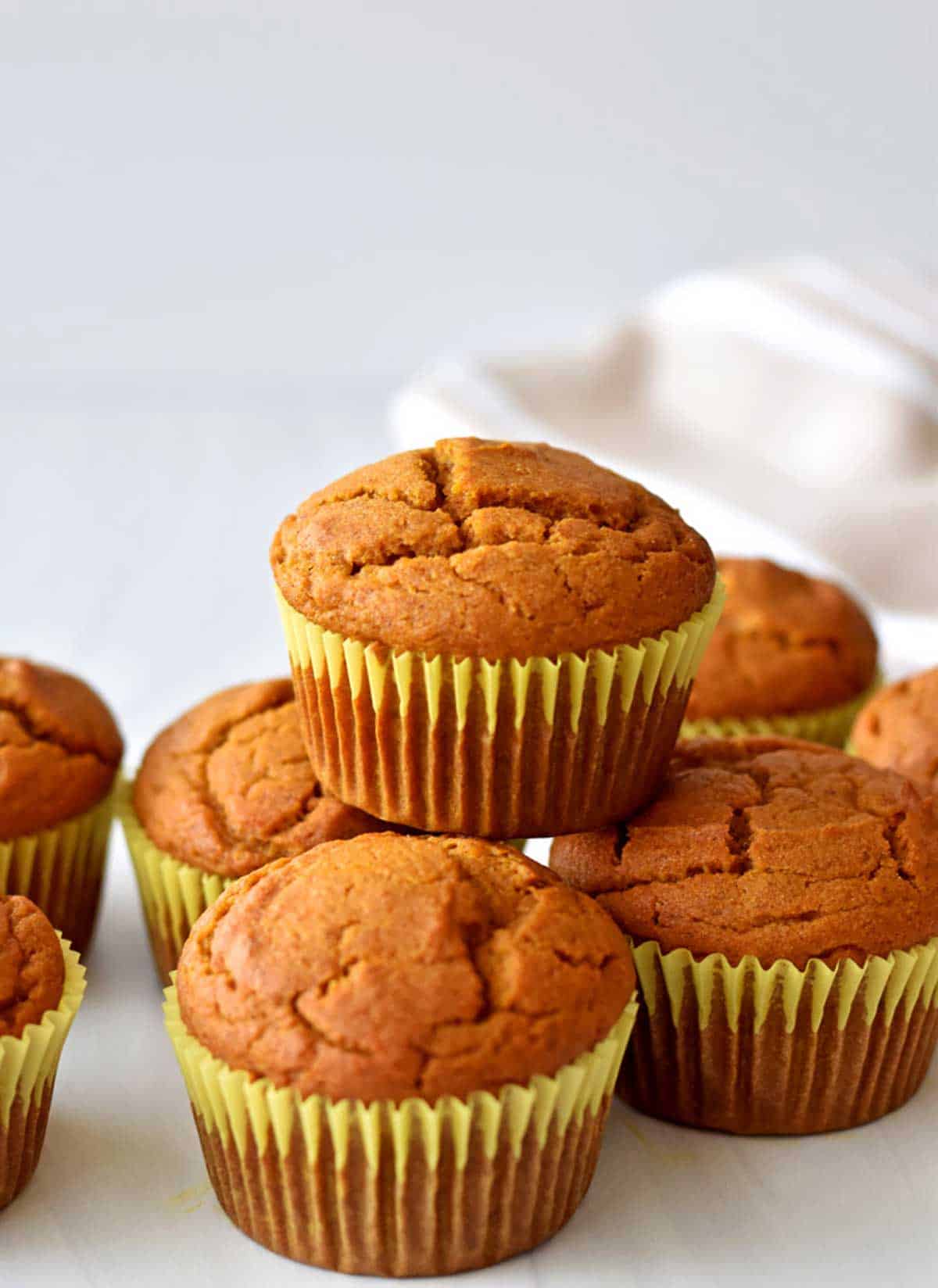 A stack of gluten free pumpkin muffins and a brown and white striped kitchen towel in the background.