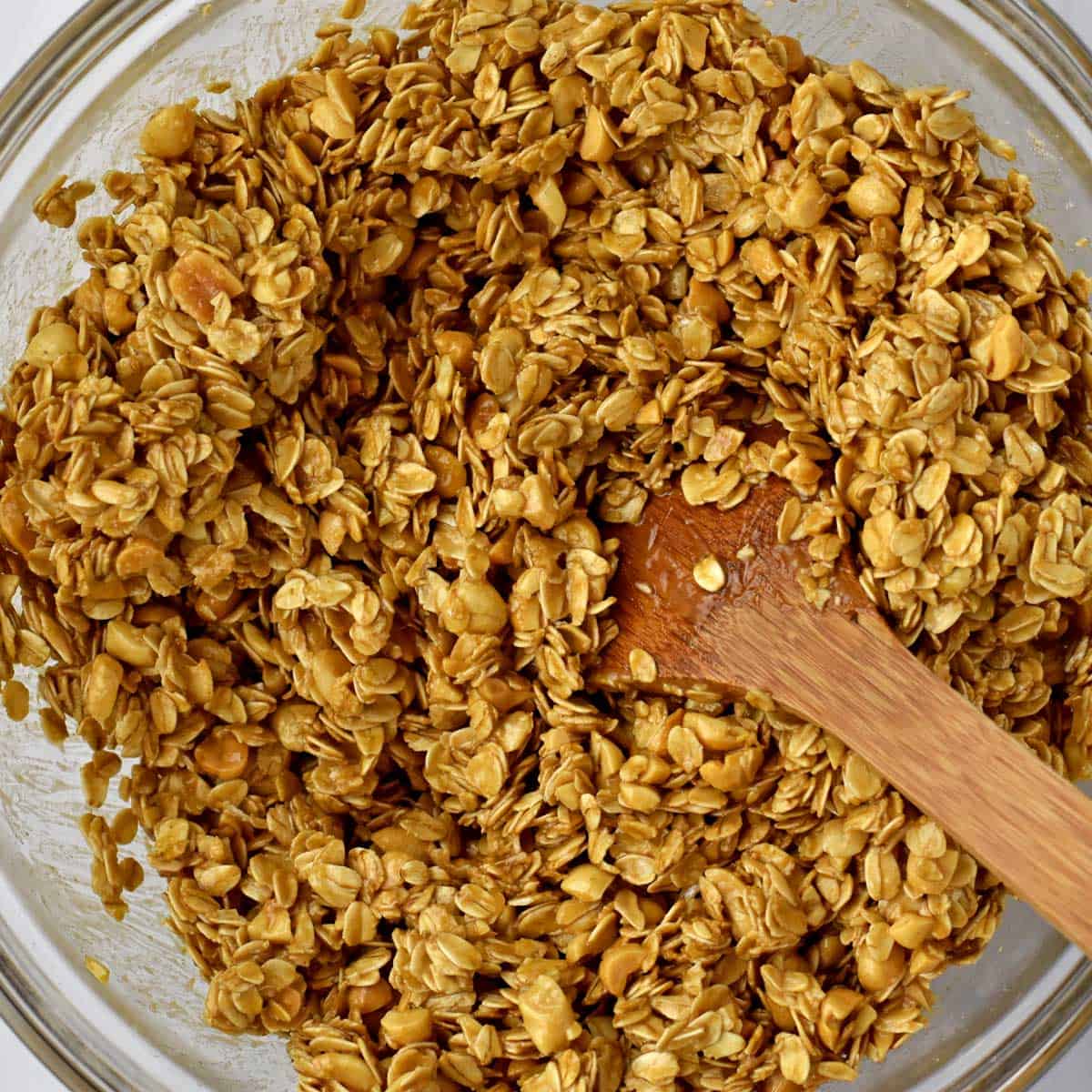 Unbaked peanut butter granola and wooden spoon in glass mixing bowl.