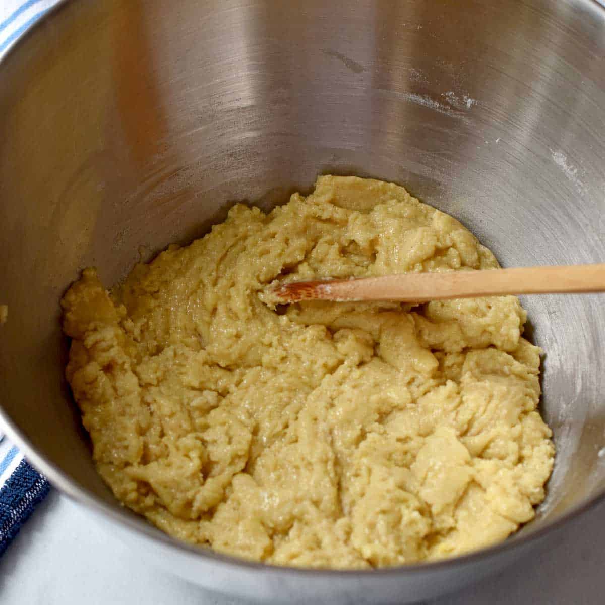 Batter for gluten free banana cake before adding the bananas and a wooden spoon in a large mixing bowl.