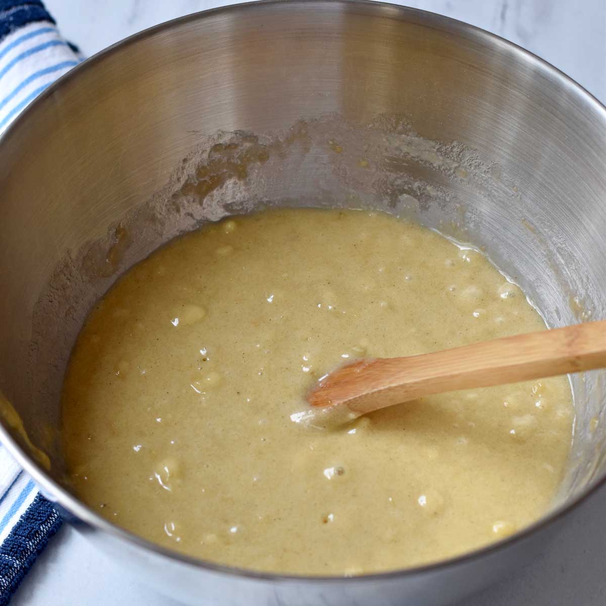 Batter for making gluten free banana cake and a wooden spoon in a large mixing bowl.