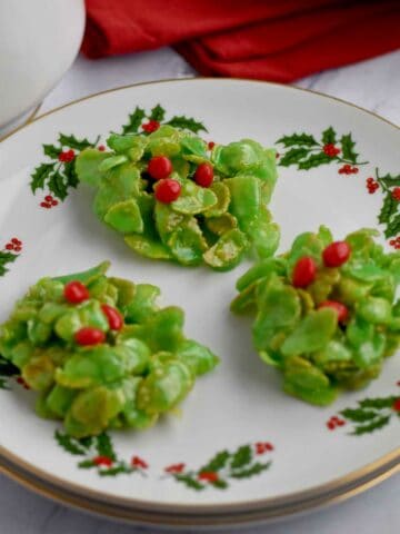 Three holly cookies on a small round plate.