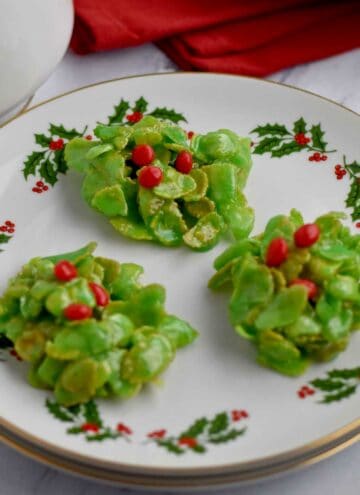 Three holly cookies on a small round plate.