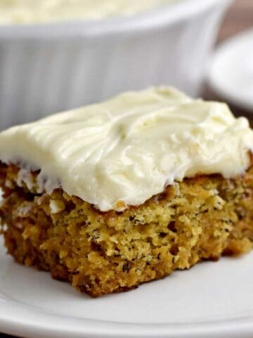 A slice of gluten free banana cake with cream cheese frosting on a white dessert plate.