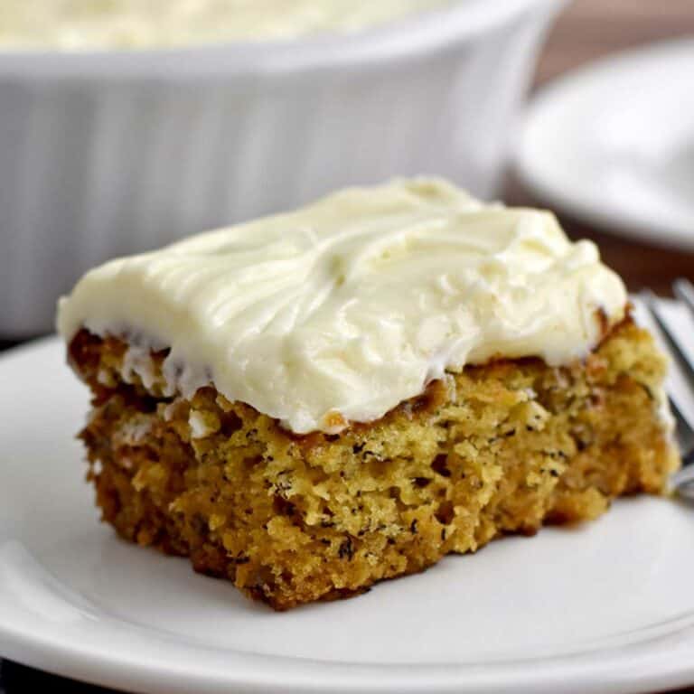 A slice of gluten free banana cake with cream cheese frosting on a white dessert plate.