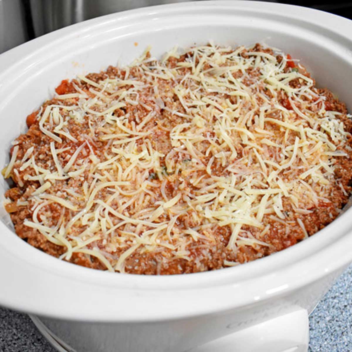 Uncooked gluten free lasagna in a white slow cooker.