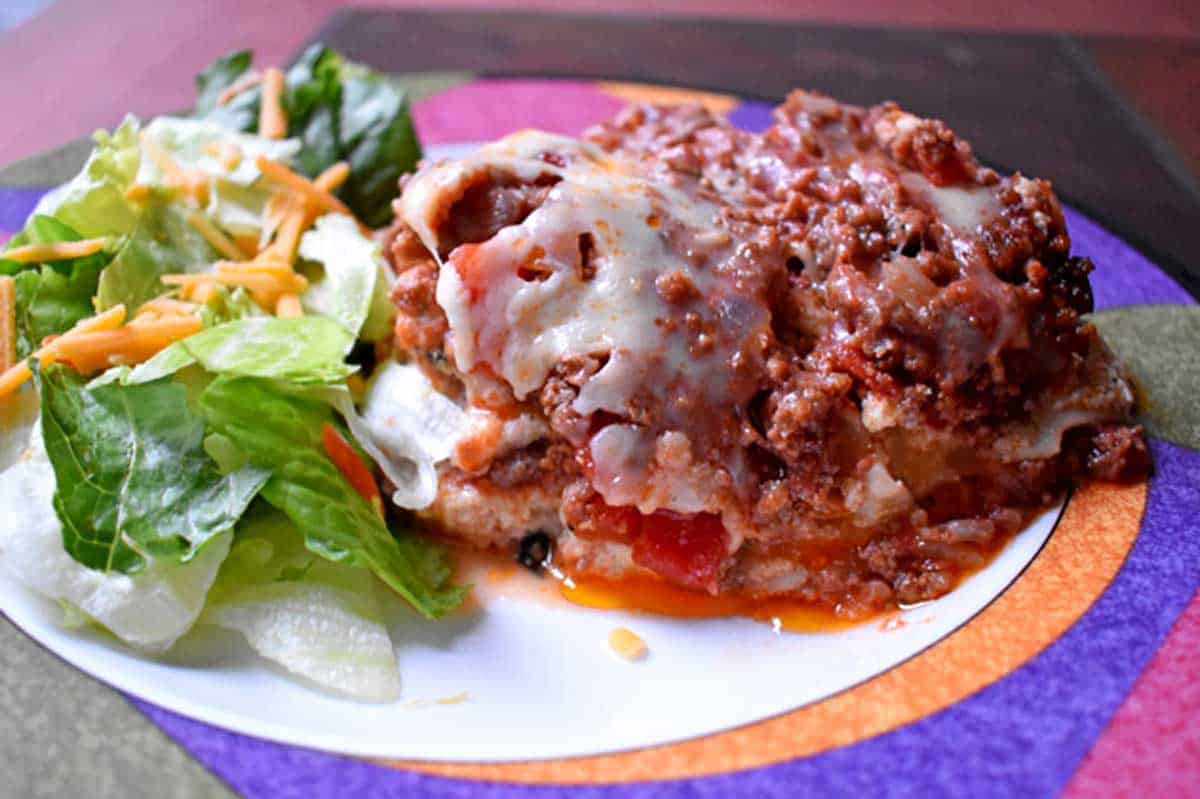 A small green salad and a serving of gluten free slow cooker lasagna on a dinner plate.