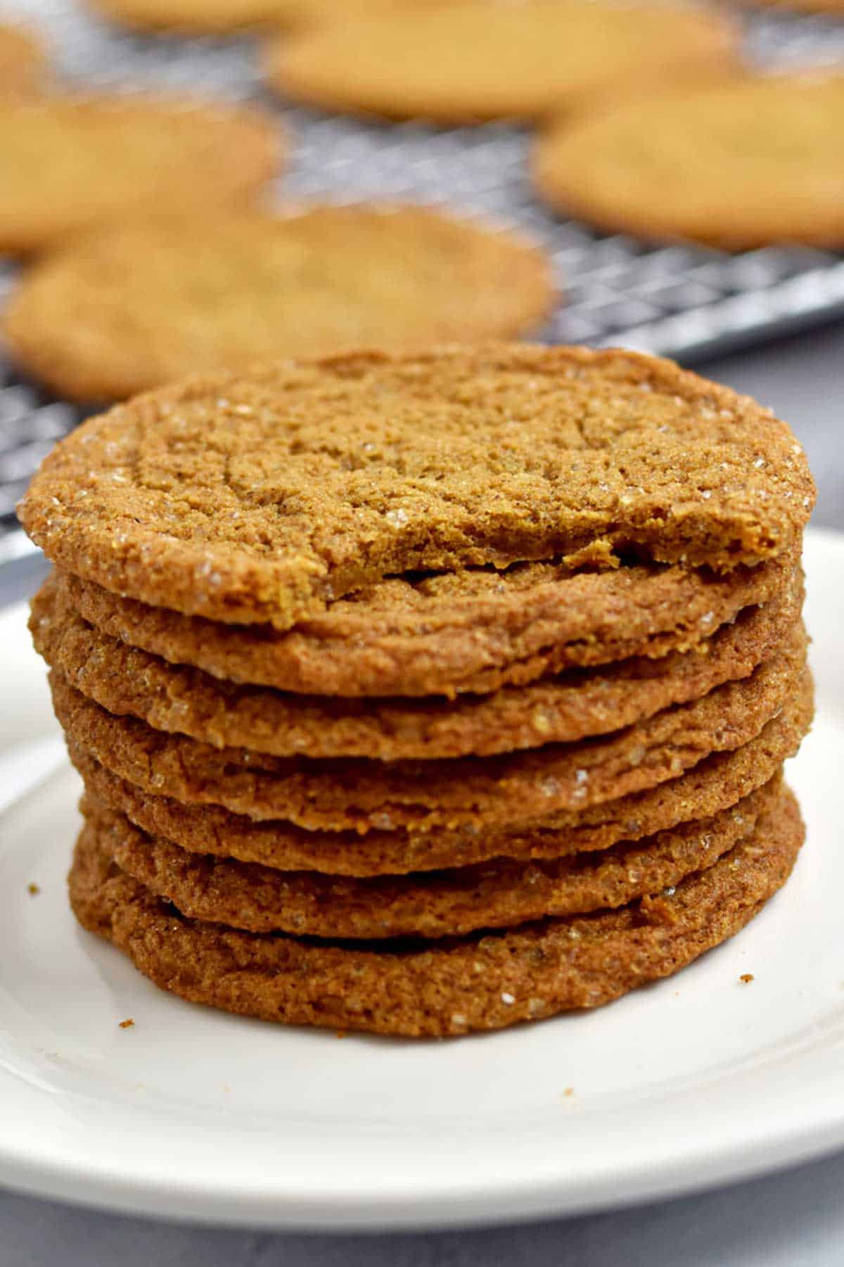 A stack of gluten free ginger snaps on a round white plate with a bite taken out of the top cookie.