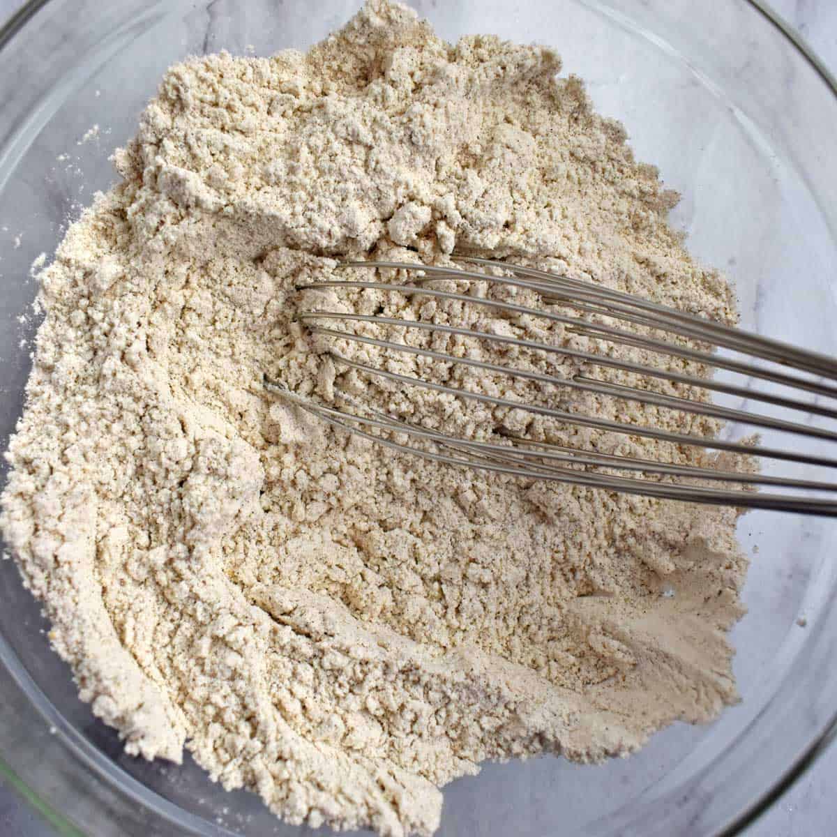 Dry ingredients for gluten free ginger snaps whisked together with a wire whisk in a glass mixing bowl.