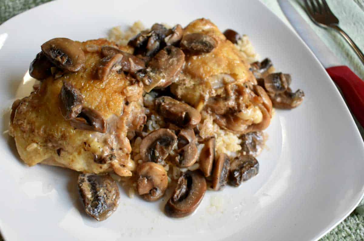 A serving of chicken marsala on a white dinner plate with silverware on the side.