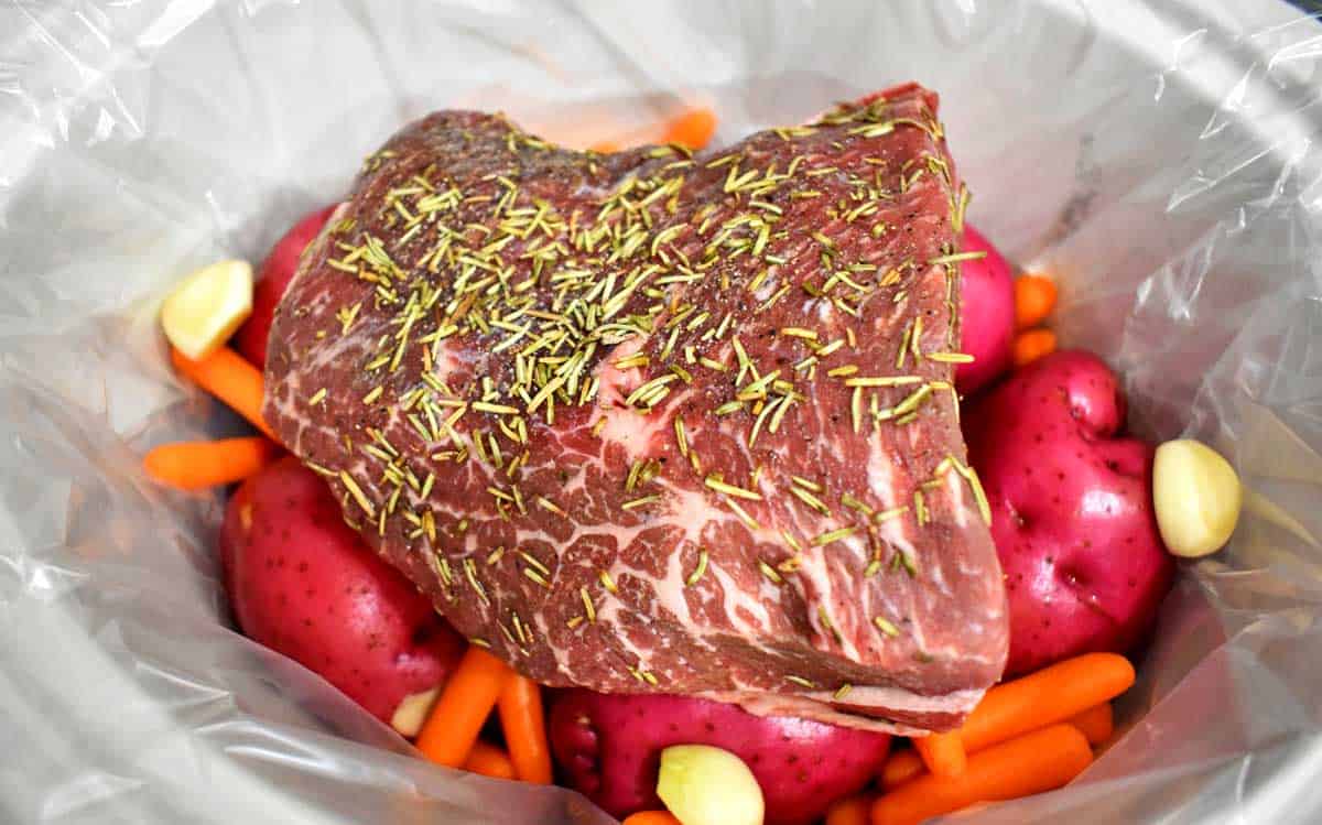 Beef pot roast and vegetables in lined crockpot ready to be slow cooked.