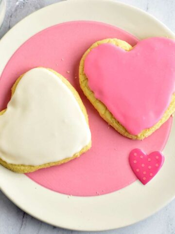 Two gluten free frosted sugar cookies on a pink and white plate.