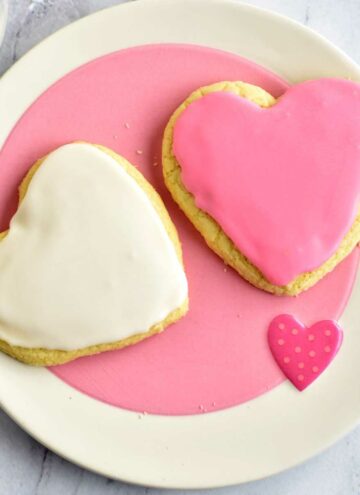 Two gluten free frosted sugar cookies on a pink and white plate.