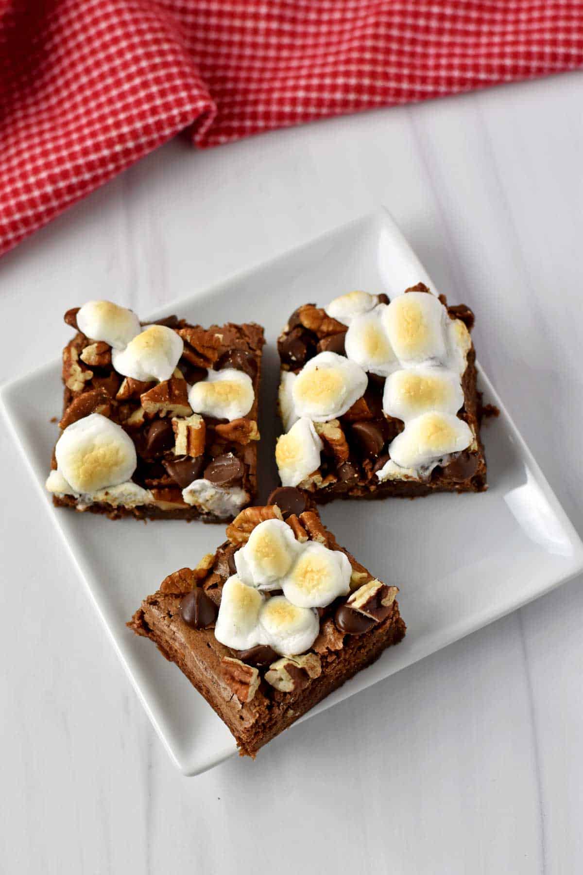 Three gluten free rocky road brownies on a small white dessert plate.