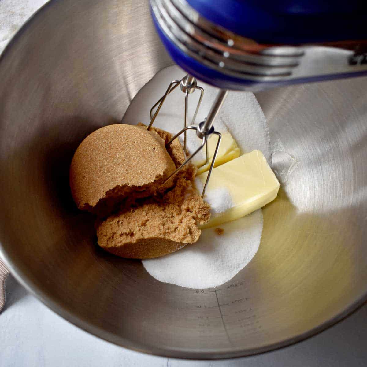 Sugars and butter being mixed together in a large metal mixing bowl.