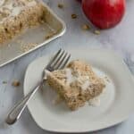 A serving of gluten free apple crumb cake and a fork on a small white plate.