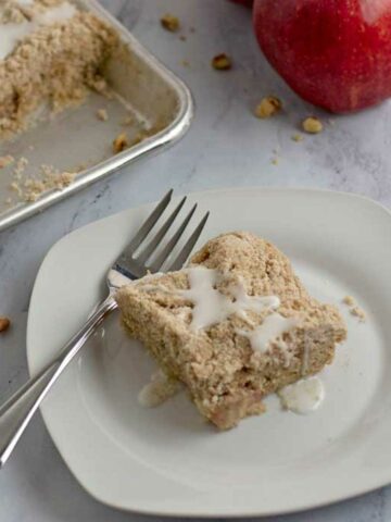 A serving of gluten free apple crumb cake and a fork on a small white plate.