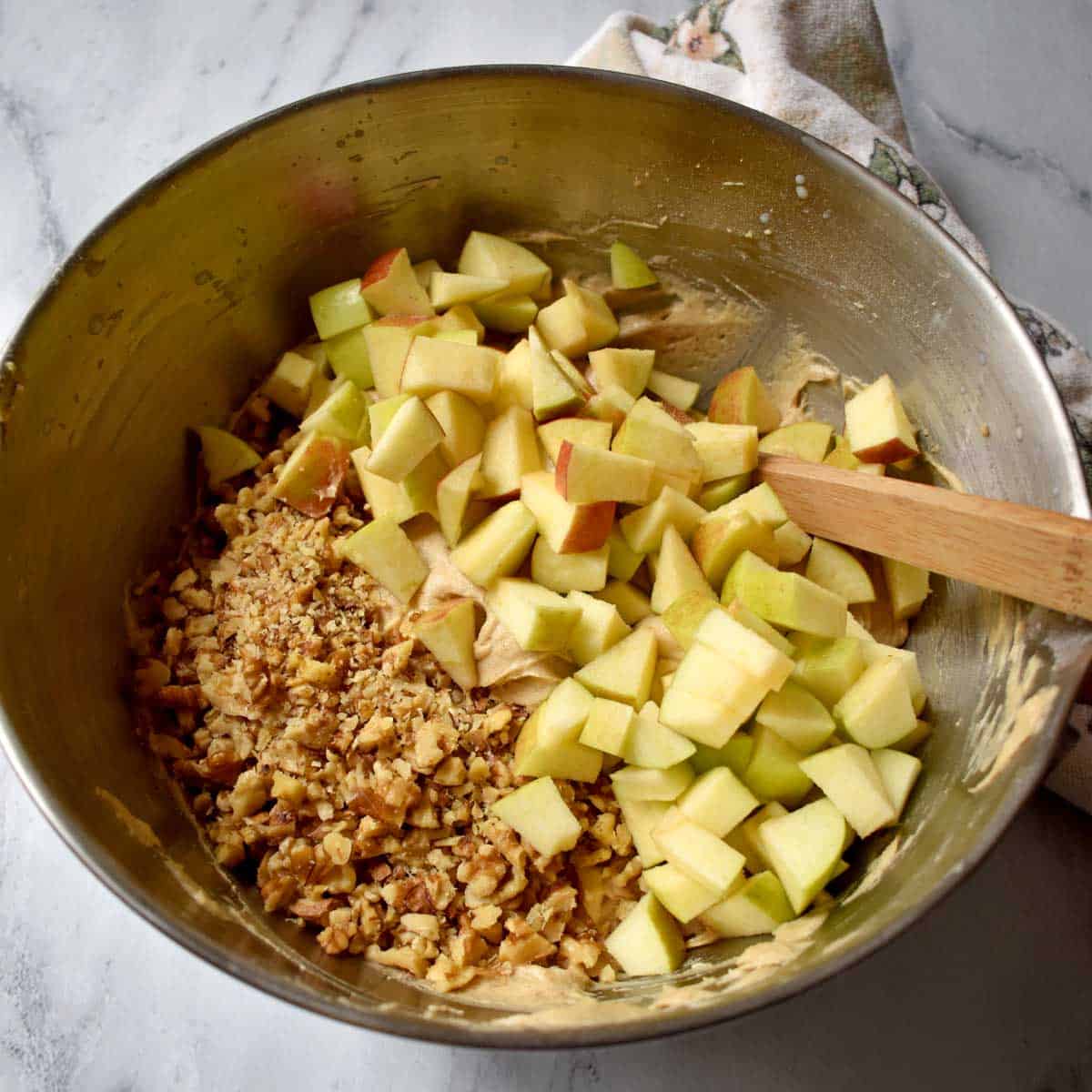 Chopped apples and walnuts being added to apple crumb cake batter.