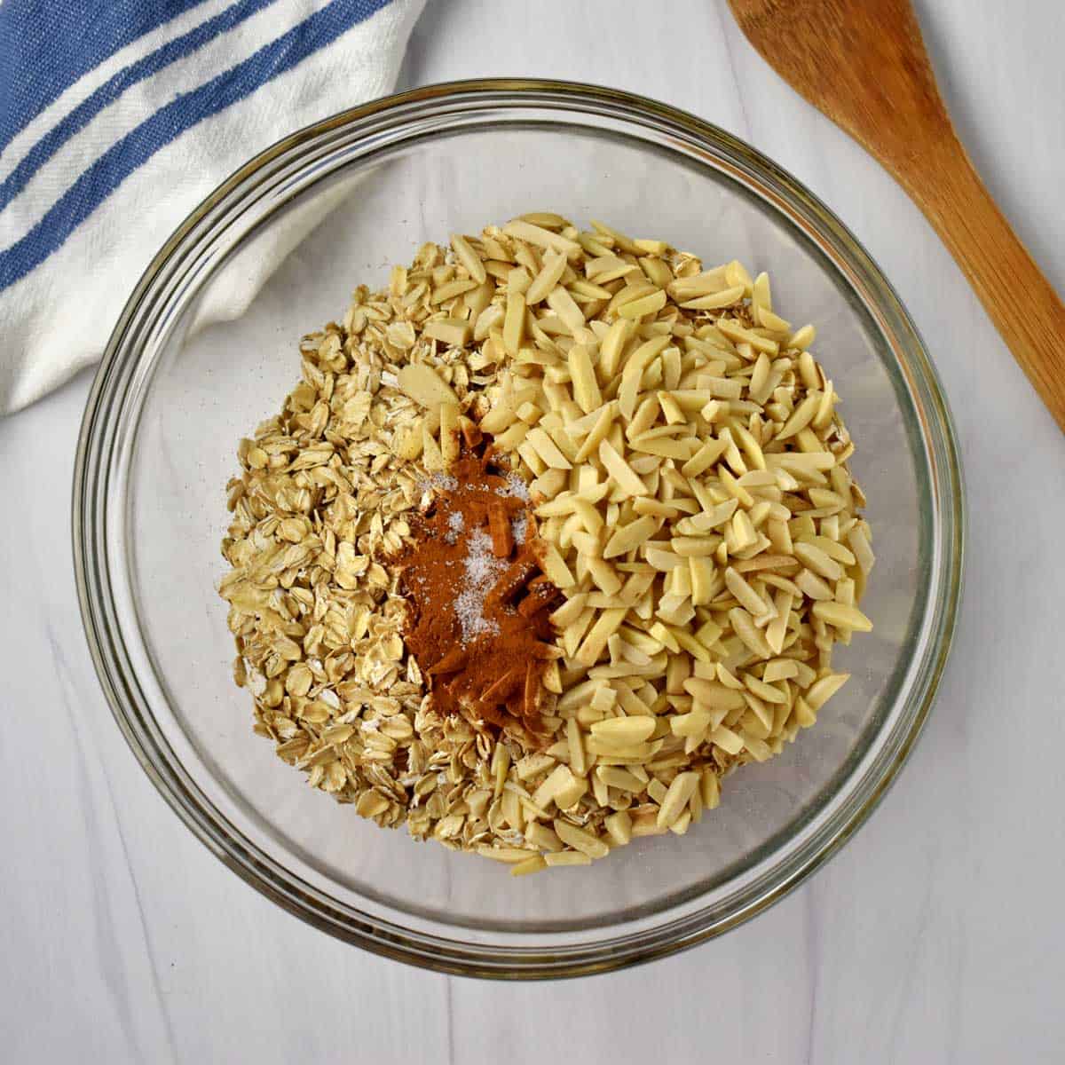 Gluten free oats, slivered almonds, cinnamon, and salt in glass mixing bowl.