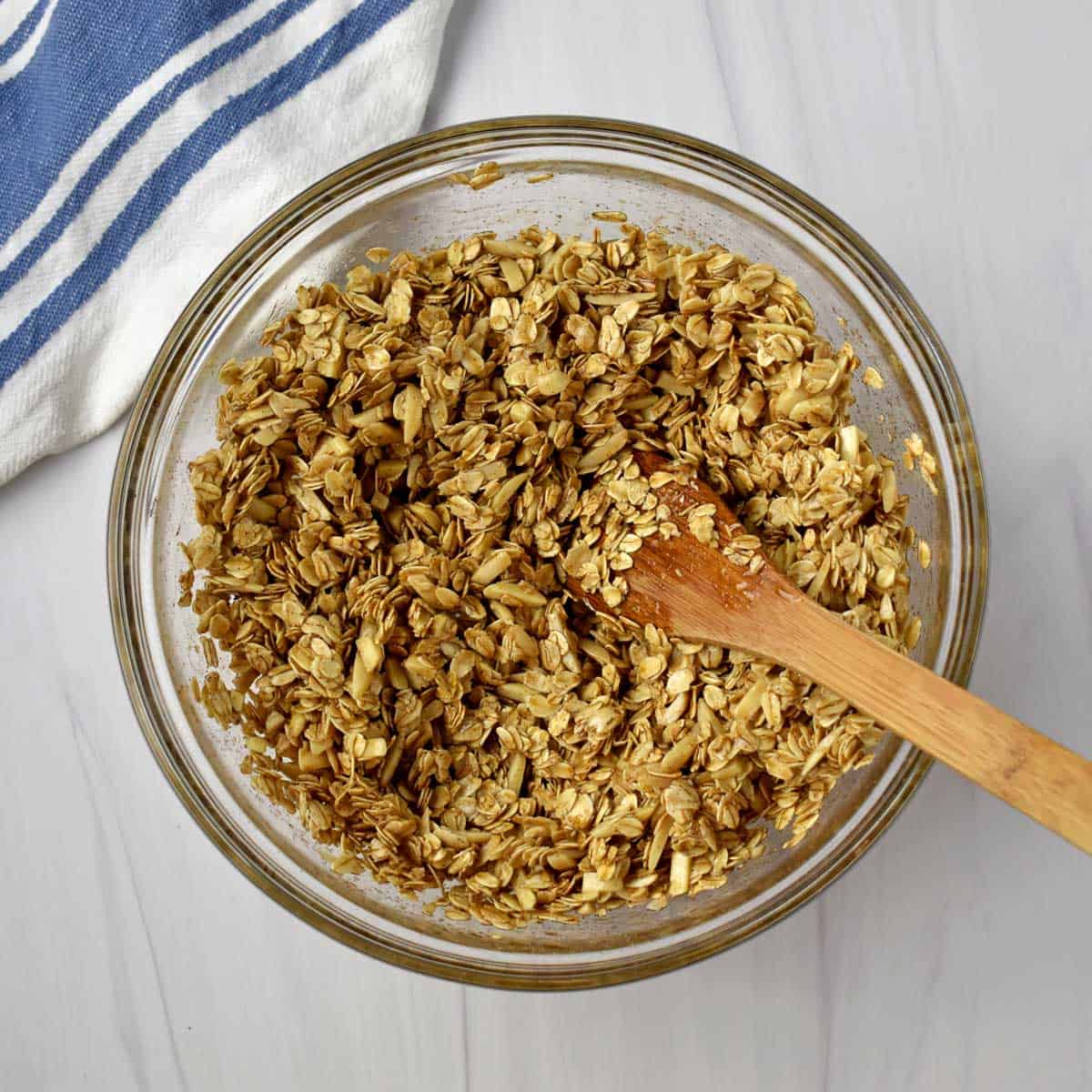 Unbaked vanilla almond granola and wooden spoon in mixing bowl.