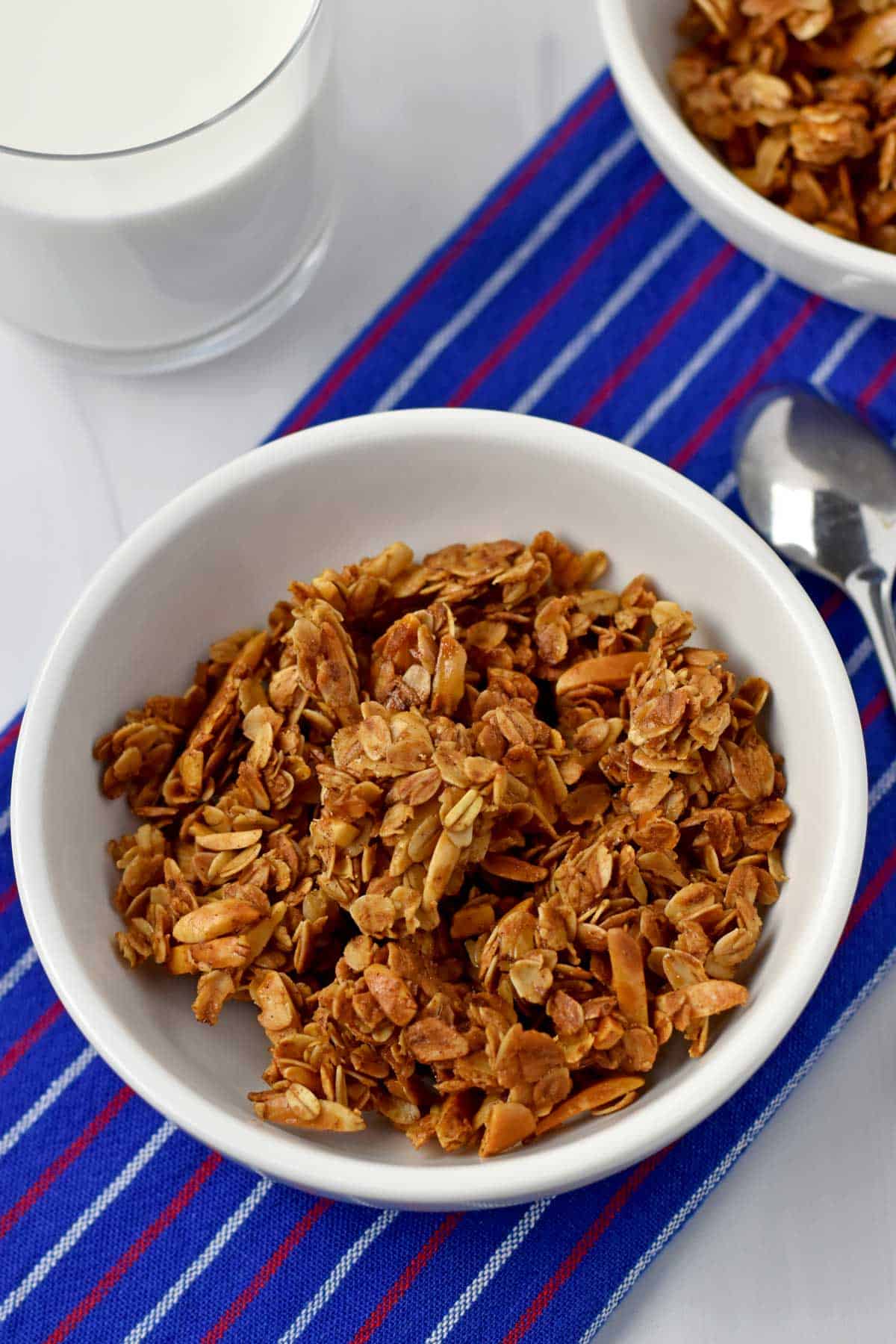 A bowl of vanilla almond granola with a glass of milk and more granola in the background.