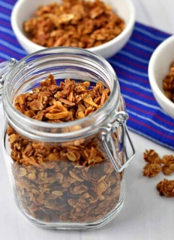 A glass jar and two cereal bowls filled with vanilla almond granola.