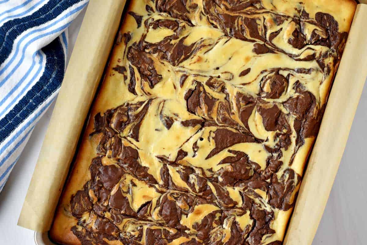 Baked gluten free cheesecake brownies in parchment lined 9x13-inch pan.